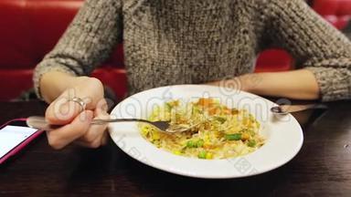 漂亮的白人女孩在咖啡馆里用手机吃泰国米饭和蔬菜。